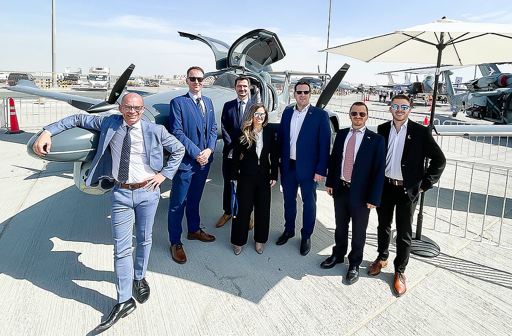 A diverse team of seven stands proudly next to a cutting-edge aircraft, reflecting a dynamic atmosphere of business and aviation excellence.