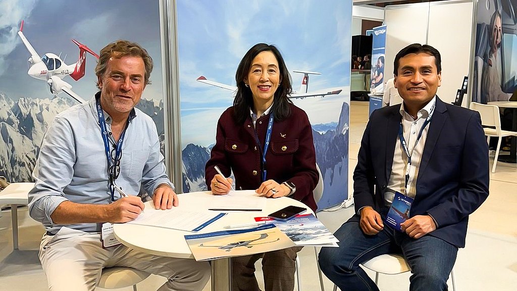 Three professionals engage in a discussion at a trade show, surrounded by aviation-themed displays and a modern booth setup.