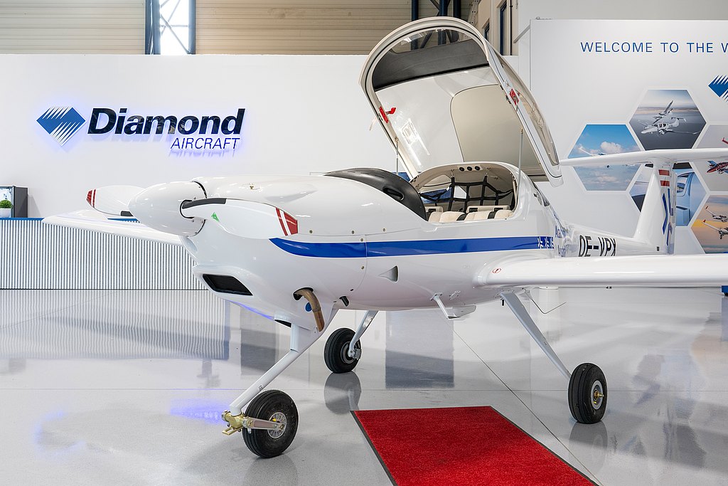 In a stylish aviation showroom, a white DA20i Katana plane with a blue accent is prominently displayed, showcasing its elegant design and features.