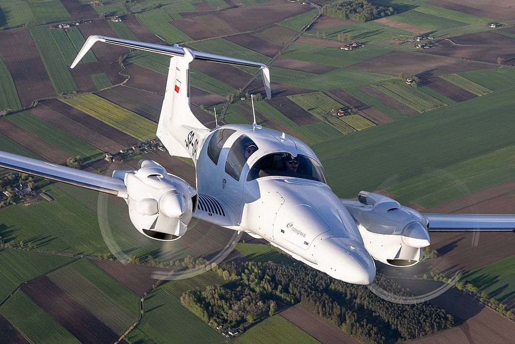 In mid-flight, a DA62 MPP twin-engine plane navigates through the air, revealing a stunning view of cultivated fields below.