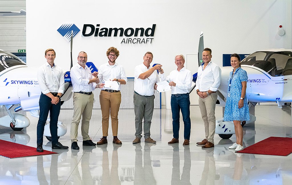 Group of people standing in front of two DA40 aircraft in a hangar.