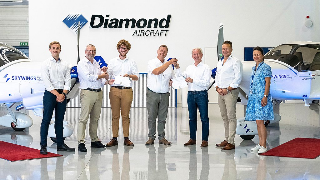 Group of people standing in front of two DA40 aircraft in a hangar.