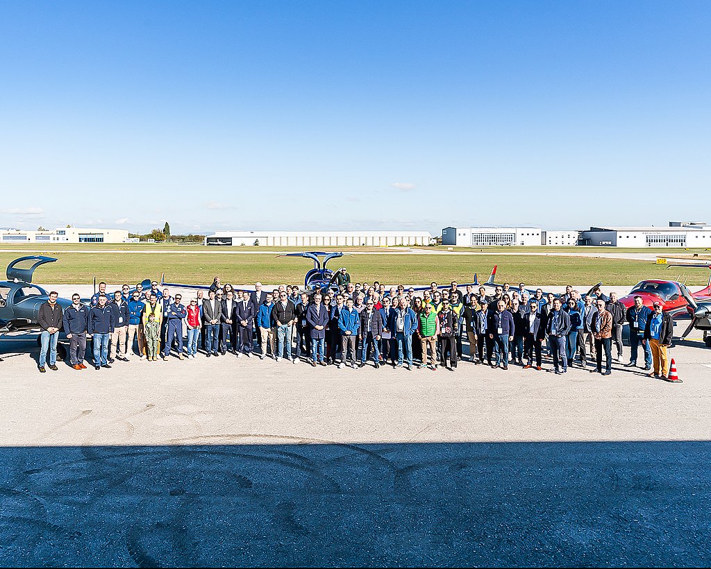 Large group of people standing in front of Diamond aircraft at the ramp.