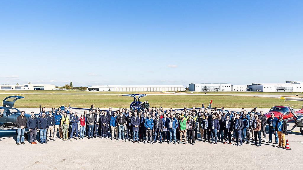 Large group of people standing in front of Diamond aircraft at the ramp.