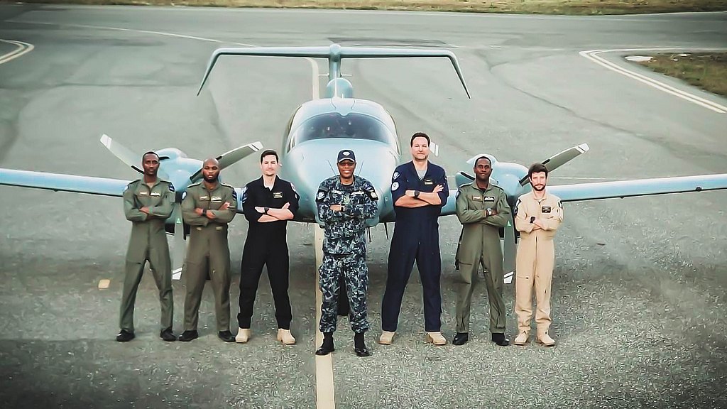 A diverse group of six pilots stands confidently in front of a DA62 MPP aircraft on a runway, showcasing camaraderie and professionalism.