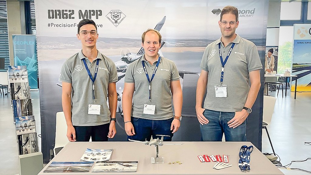 Three Diamond Aircraft employees stanind at a booth.