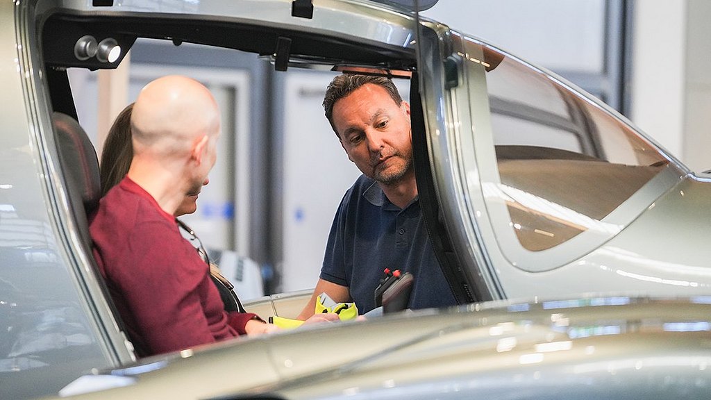 Inside a sleek aircraft, a pilot engages with two individuals, discussing controls and features with focused expressions.