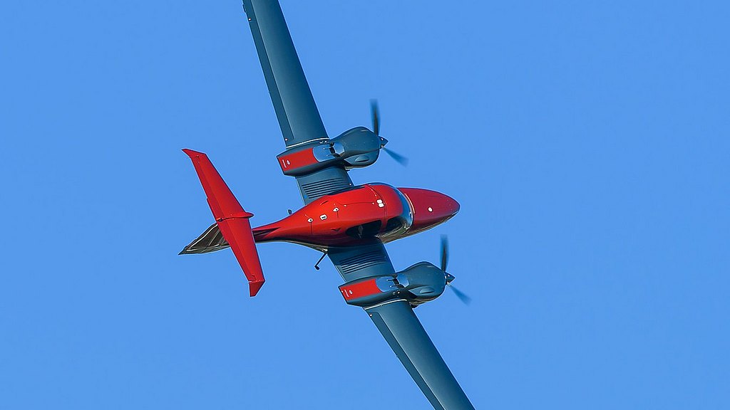 Orange DA42-VI flying in blue sky. 