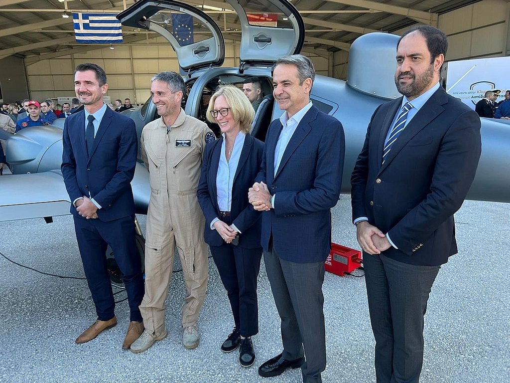 A group of five individuals stands in front of a sleek aircraft, smiling and dressed in formal attire.