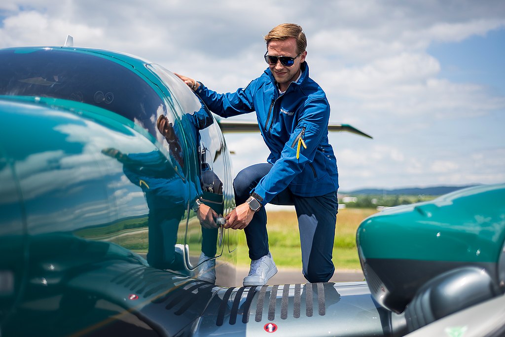 Yound men wearing a softshell jacket steps up the wing to open the door of a green DA62.