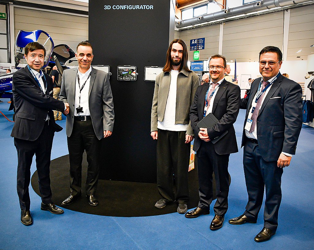 A group of four men stand together, smiling, in front of a display labeled '3D CONFIGURATOR' at an event.