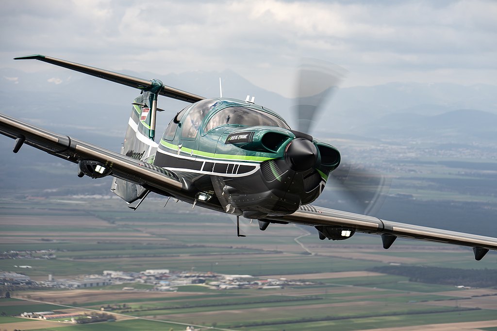 This image features a stylish DA50 RG aircraft in flight, highlighting its unique color scheme and the expansive landscape beneath it.
