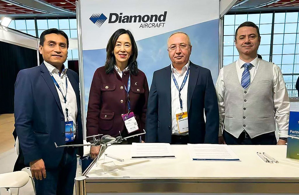 Four professionals stand together at a trade show booth, showcasing a model aircraft and engaging in conversation.