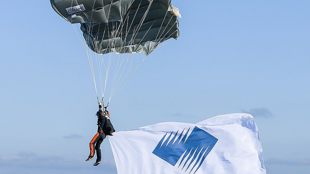 Parachutists flying with a Diamond Aircraft flag.