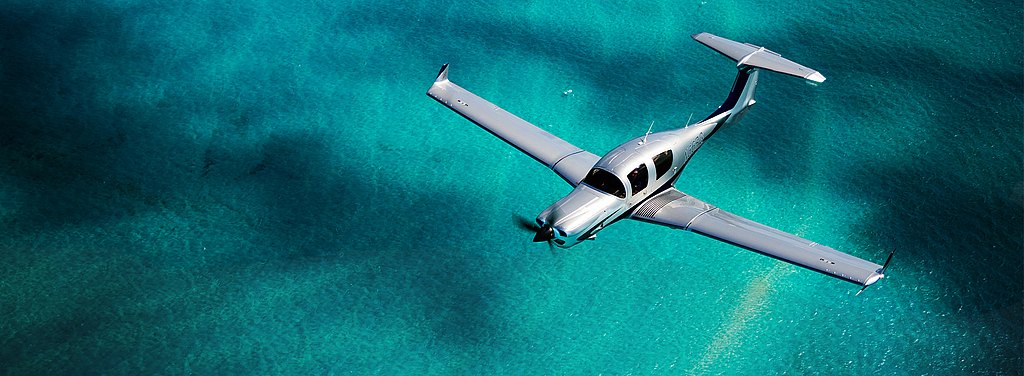 Silver DA50 RG flying over turquoise water. Silver DA50 RG flying over turquoise water.
