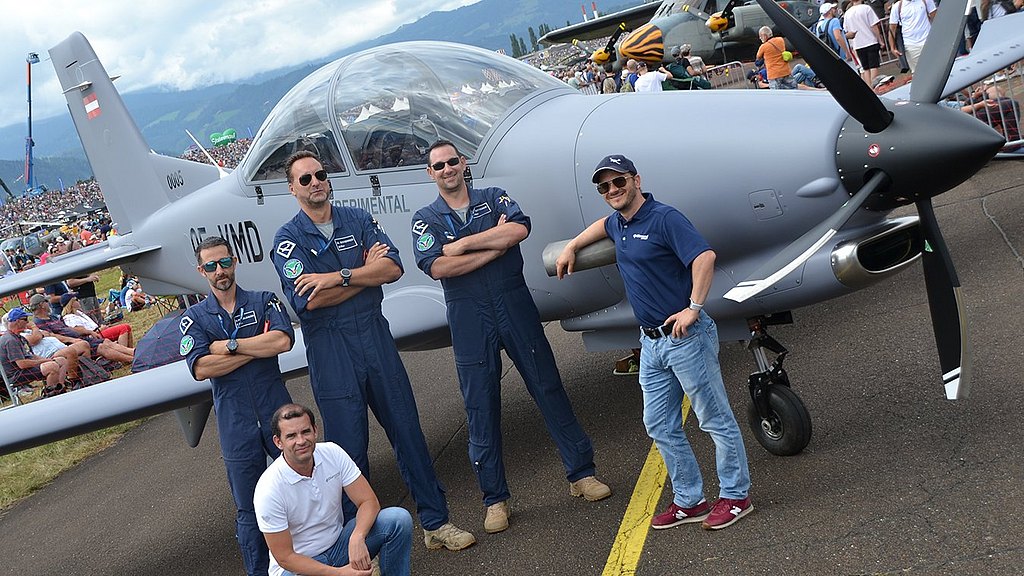 Men standing infront of DART aircraft on static display with crowd in the background.