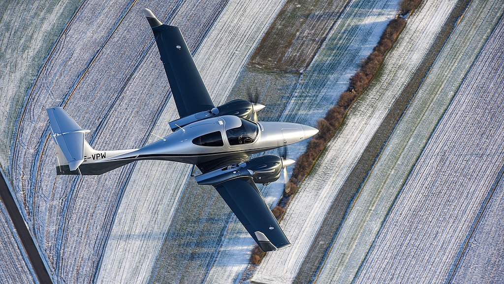 Silver DA42-VI soaring over snowy fields.