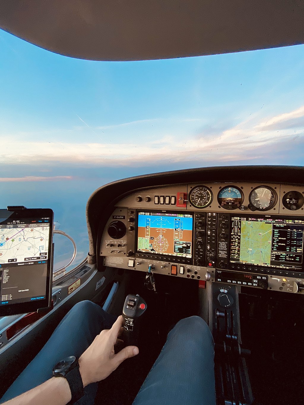 Inside the cockpit of an aircraft, a pilot grips the control stick while monitoring various instruments and screens.