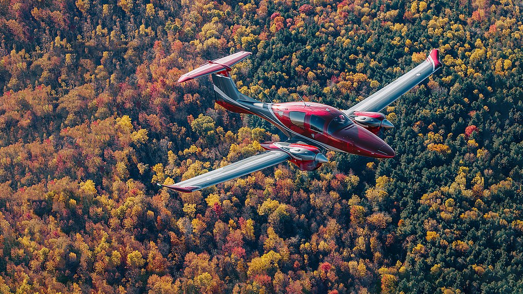 Red and anthracite DA62 flying over orange colored forrest.