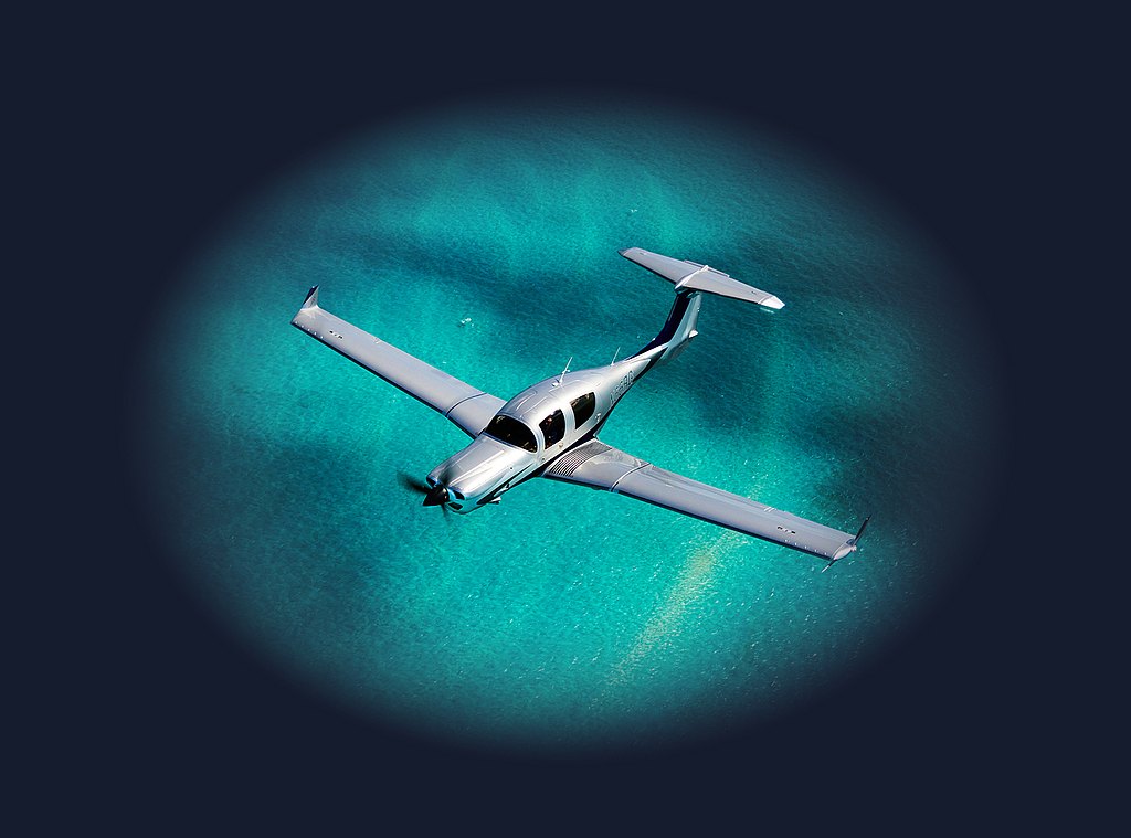 Silver DA50 RG flying over turquoise water.