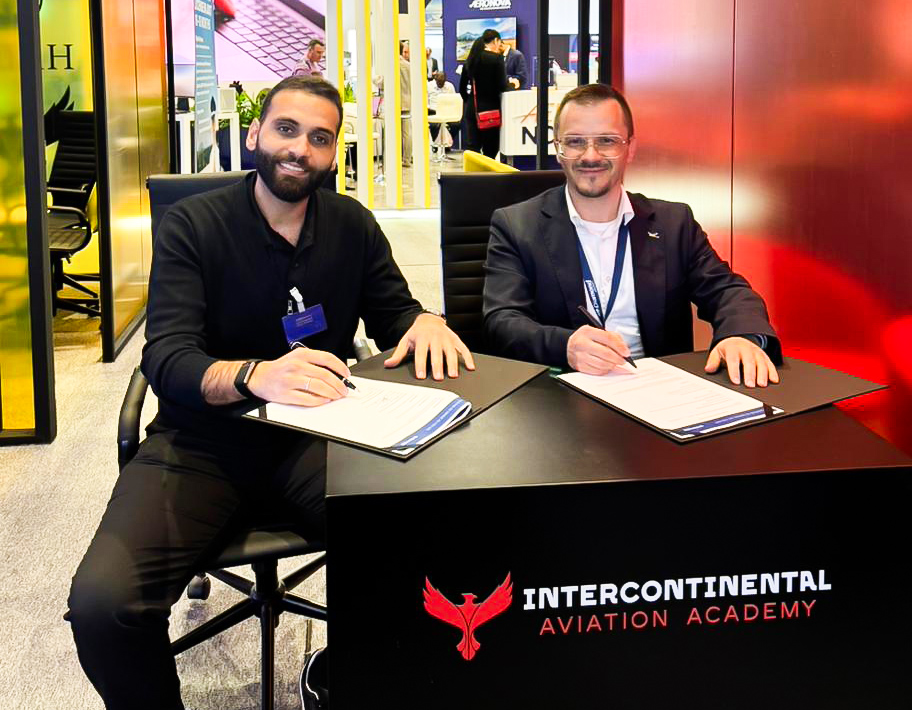 Two men sit at a table, signing documents for the Intercontinental Aviation Academy, smiling and engaged in conversation.